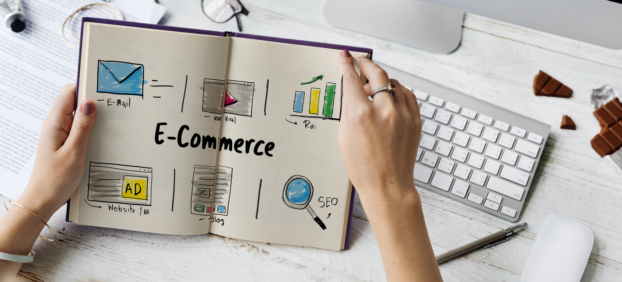 Mains tenant un carnet ouvert sur des icônes E-Commerce